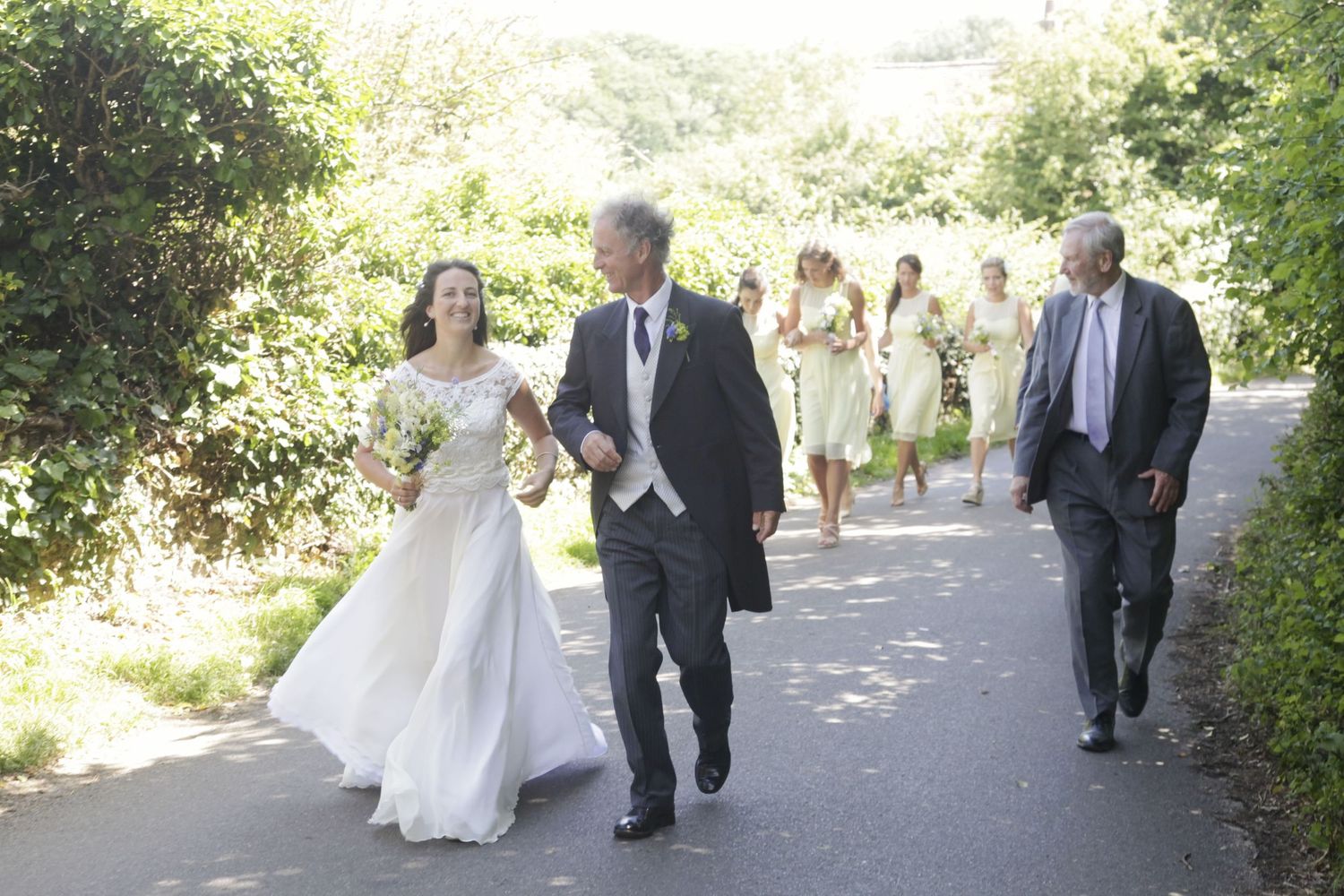 Wedding procession walking along a scenic pathway with green hills in the background.