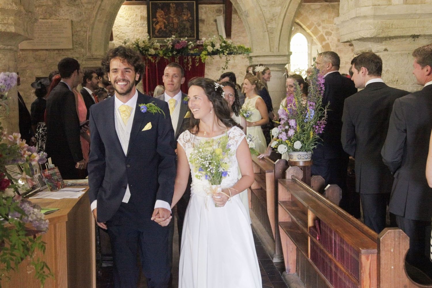 Wedding party and guests gathered in historic church hallway with stone architecture.