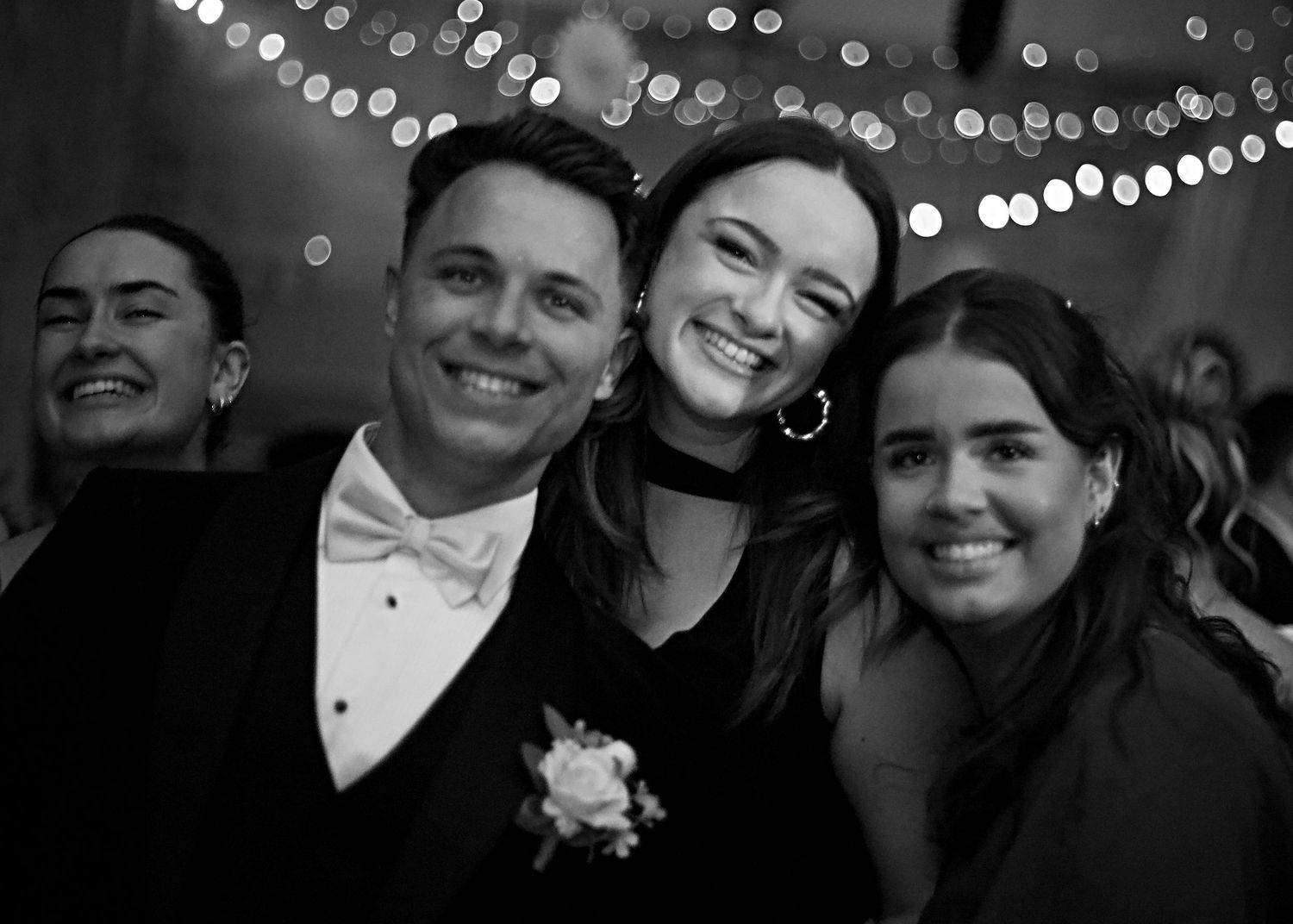 Wedding celebration captured in black and white with string lights in background.