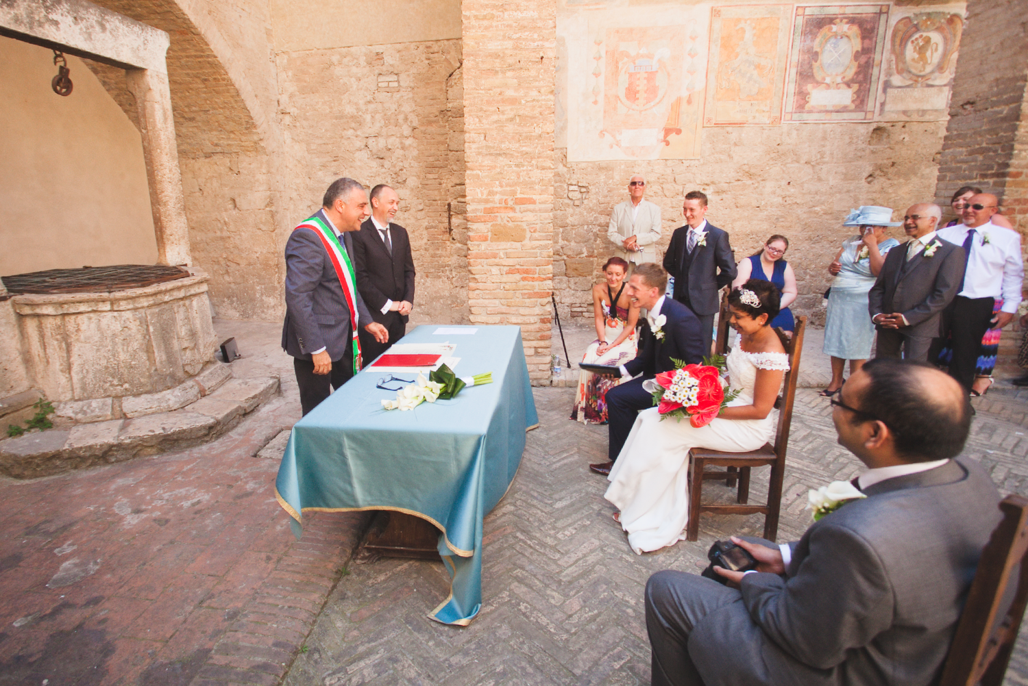 Wedding party poses for photos in a beautiful stone courtyard with arched architecture.