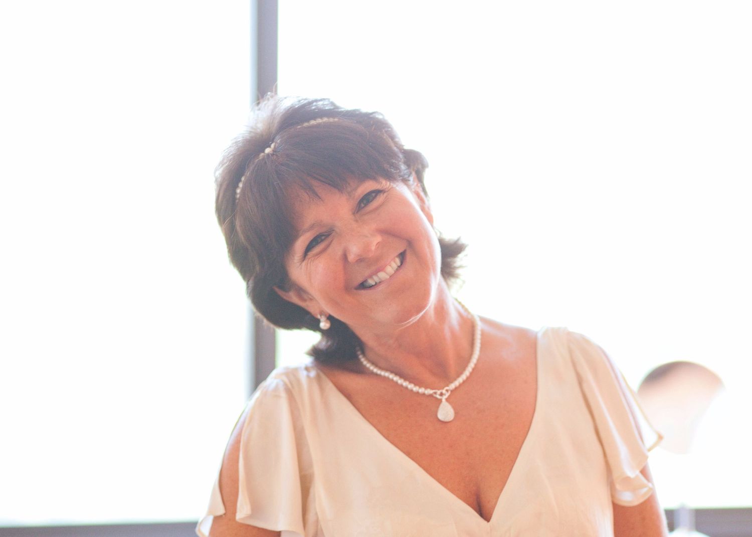 Smiling bride in a white dress holding a colorful bouquet against a bright interior background.