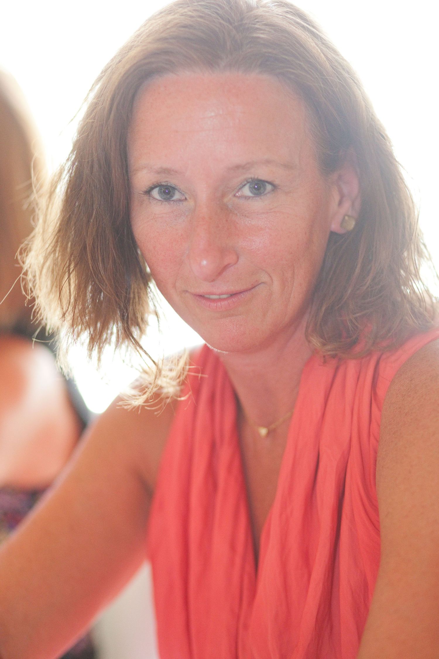 Woman in coral dress smiles warmly in soft natural lighting.