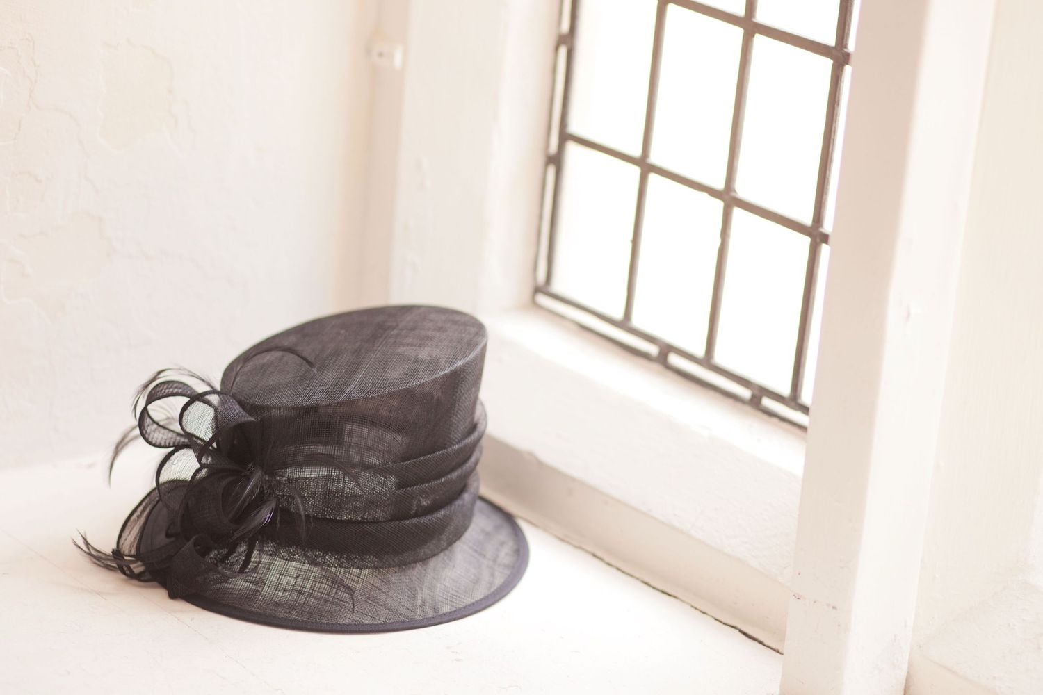 Black formal hats displayed near bright windows in an elegant white interior space.
