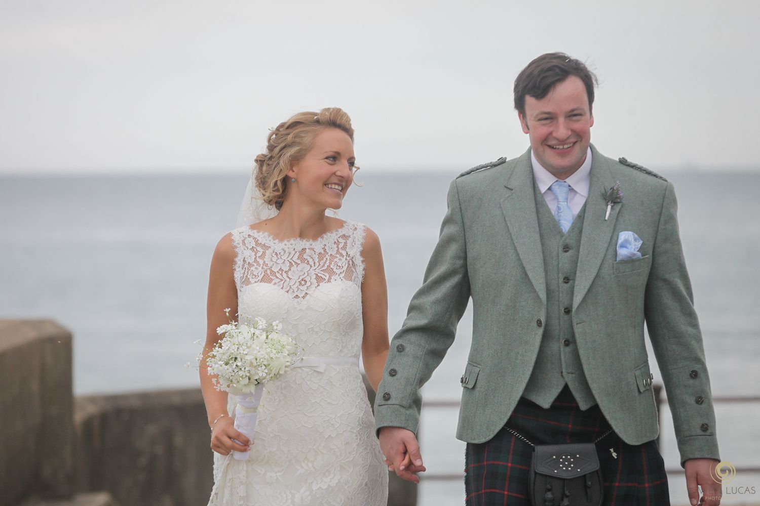 A joyful wedding couple walks together along a seaside path.