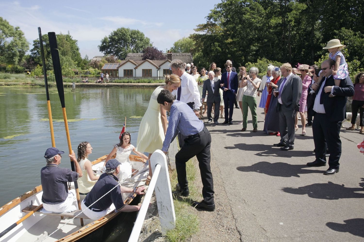 Guests gather along a lakeside path to watch a boat arrival during an outdoor celebration.