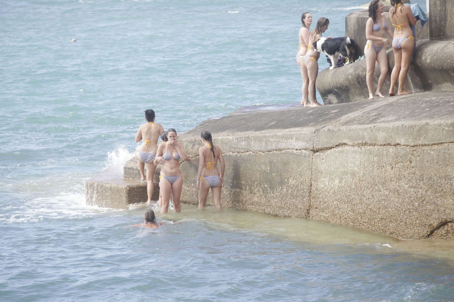 Swimmers enjoying the ocean waves near a concrete seawall on a bright day.