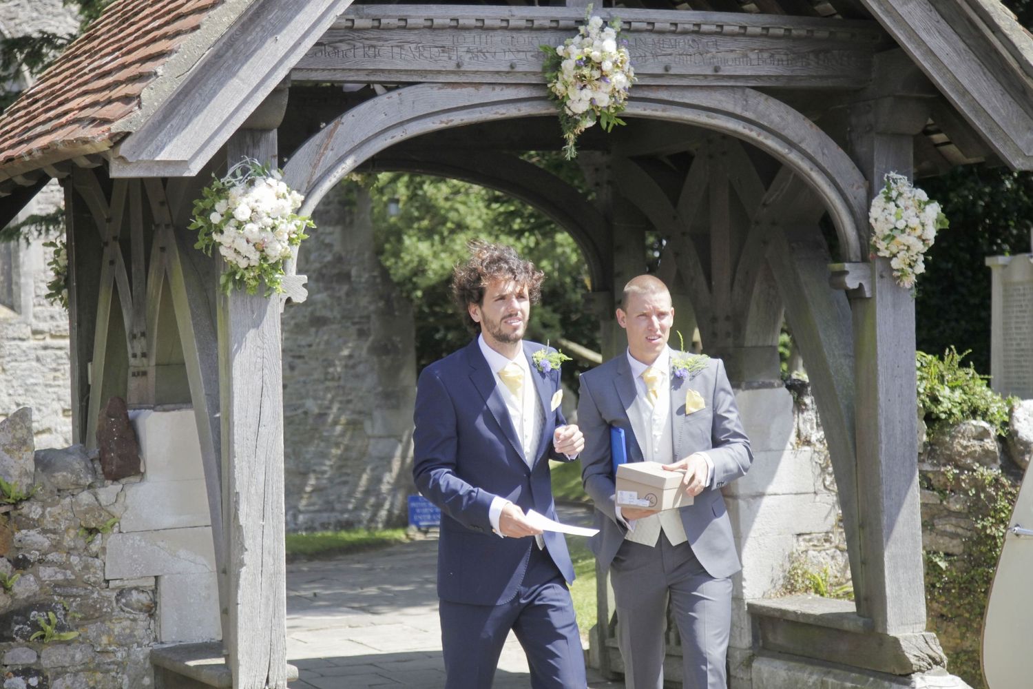 Guests in navy suits conversing under a stone archway at an outdoor event.