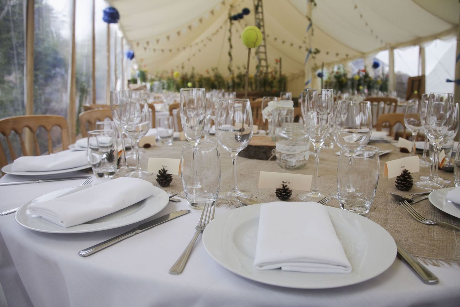 Elegant table settings with wine glasses and place cards under a white tent.