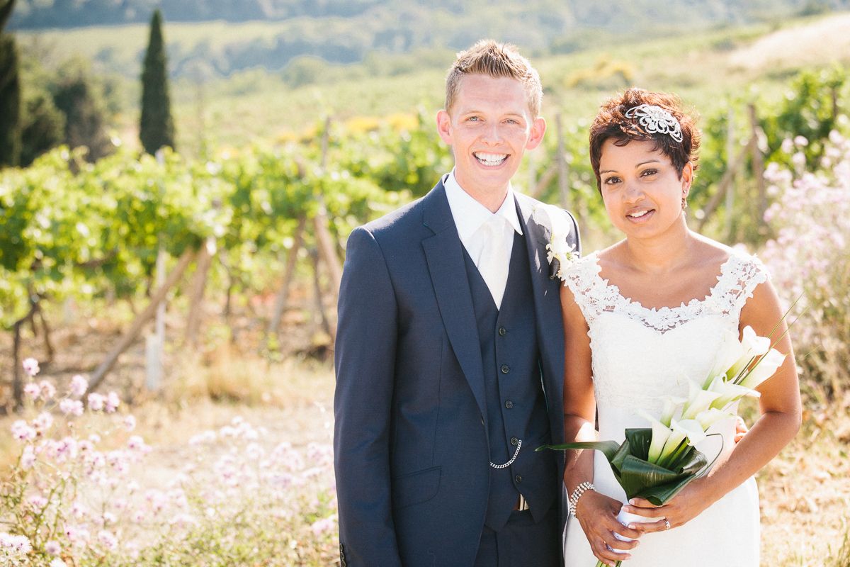 Wedding couple poses in front of a scenic vineyard on a sunny summer day in San Gimingnano, Tusacany, Italy.