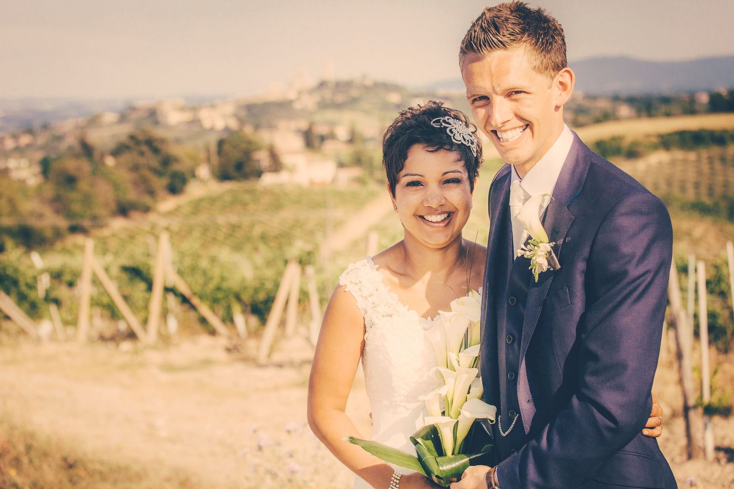 Wedding portrait in warm sunlight with vineyard landscape backdrop in San Gimingnano, Tuscany, Italy.