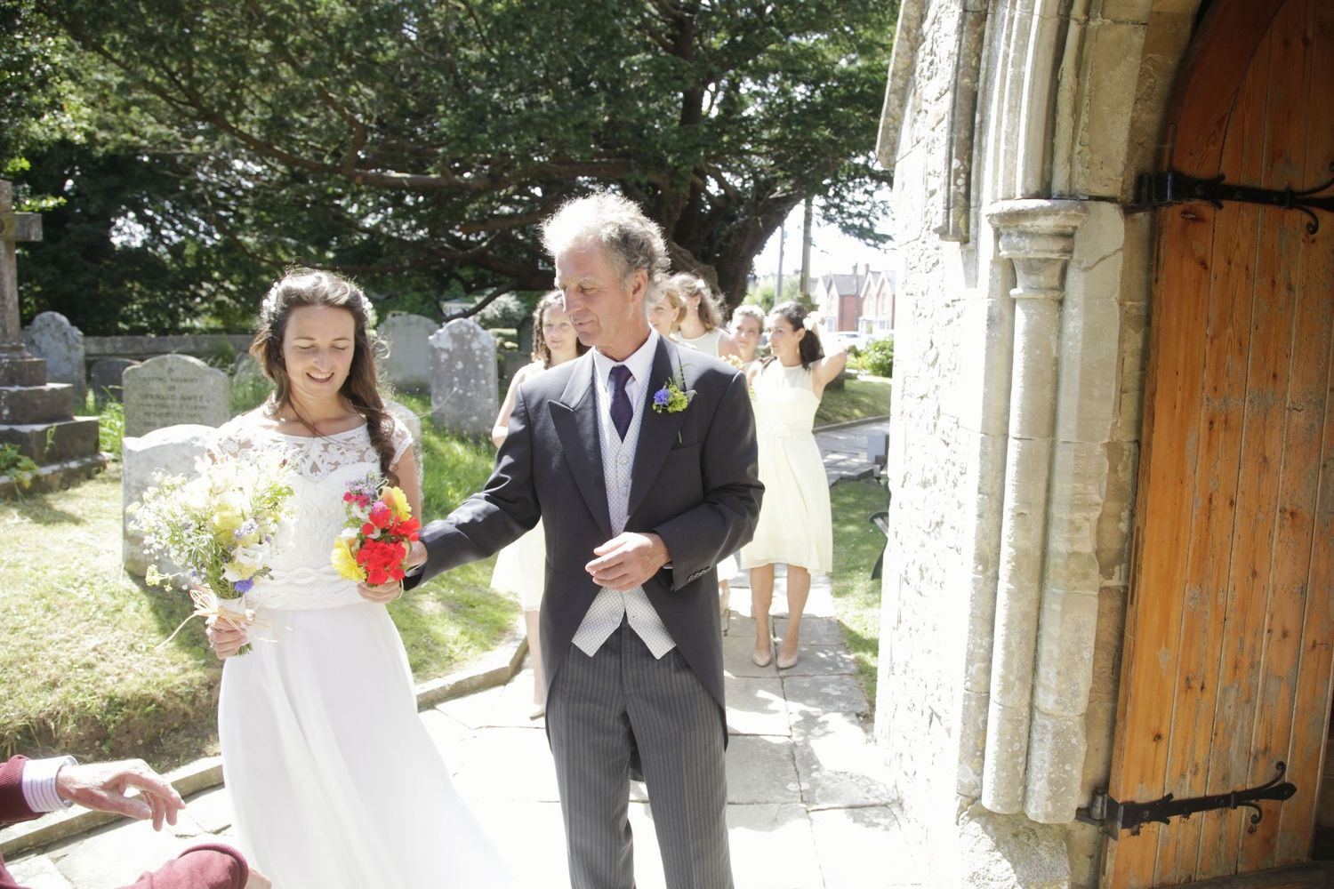 Couple exiting stone church doorway with sunlit garden in background.