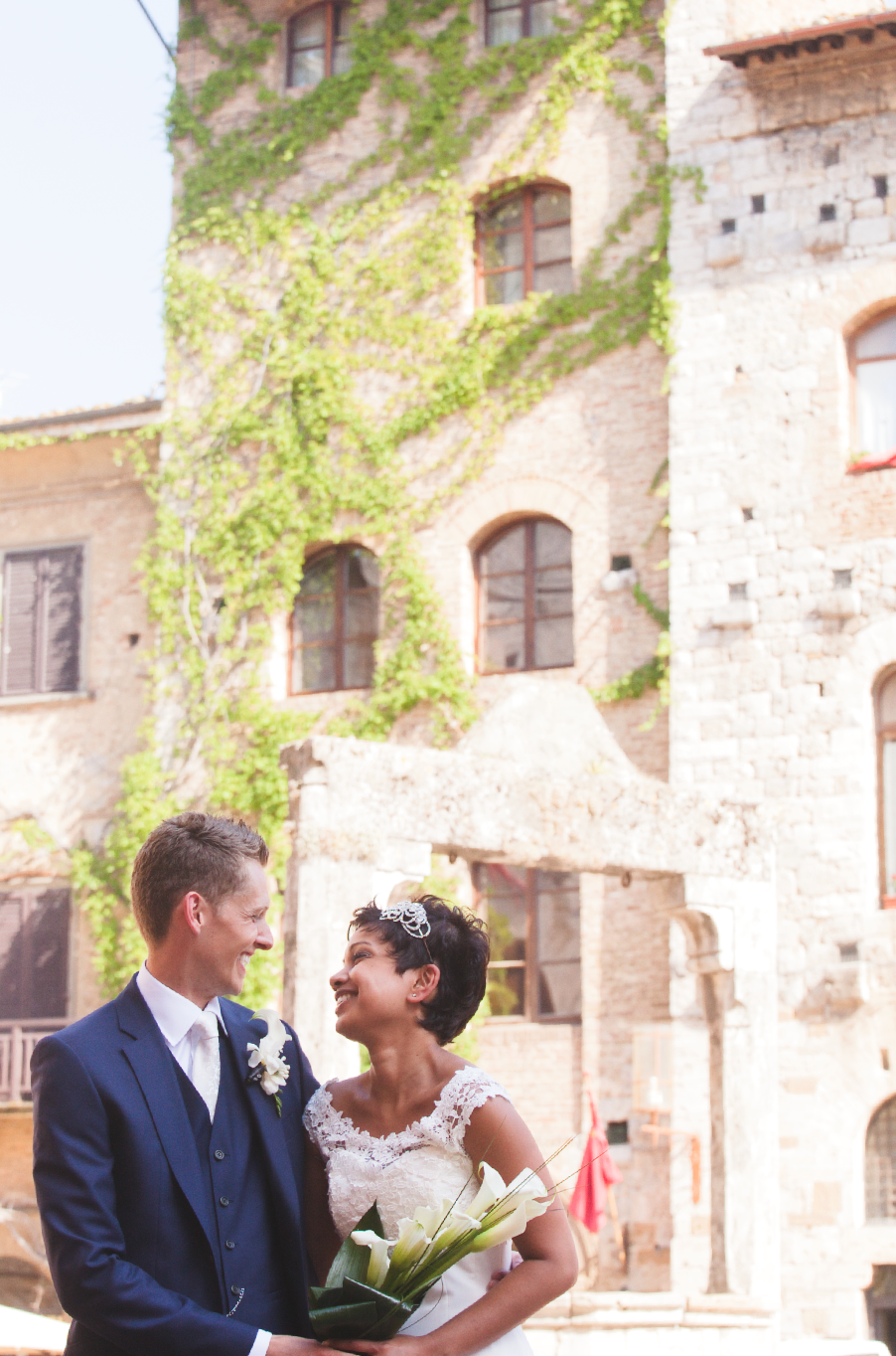 Wedding couple shares intimate moment against rustic stone wall with ivy.