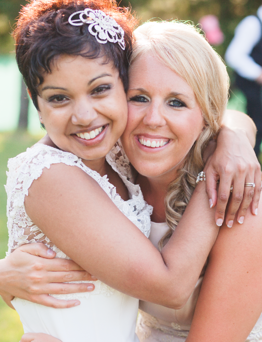 Two wedding guests embrace and smile warmly for the camera.
