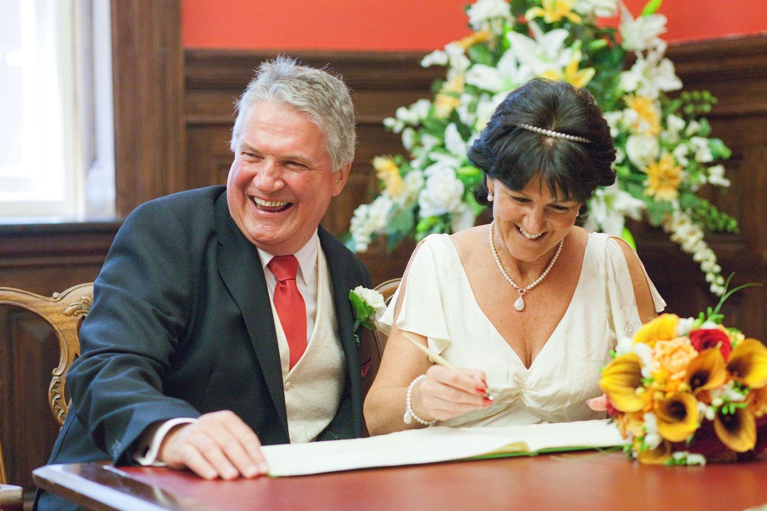 Newlyweds signing marriage documents with bright sunflower bouquet on ceremonial table.
