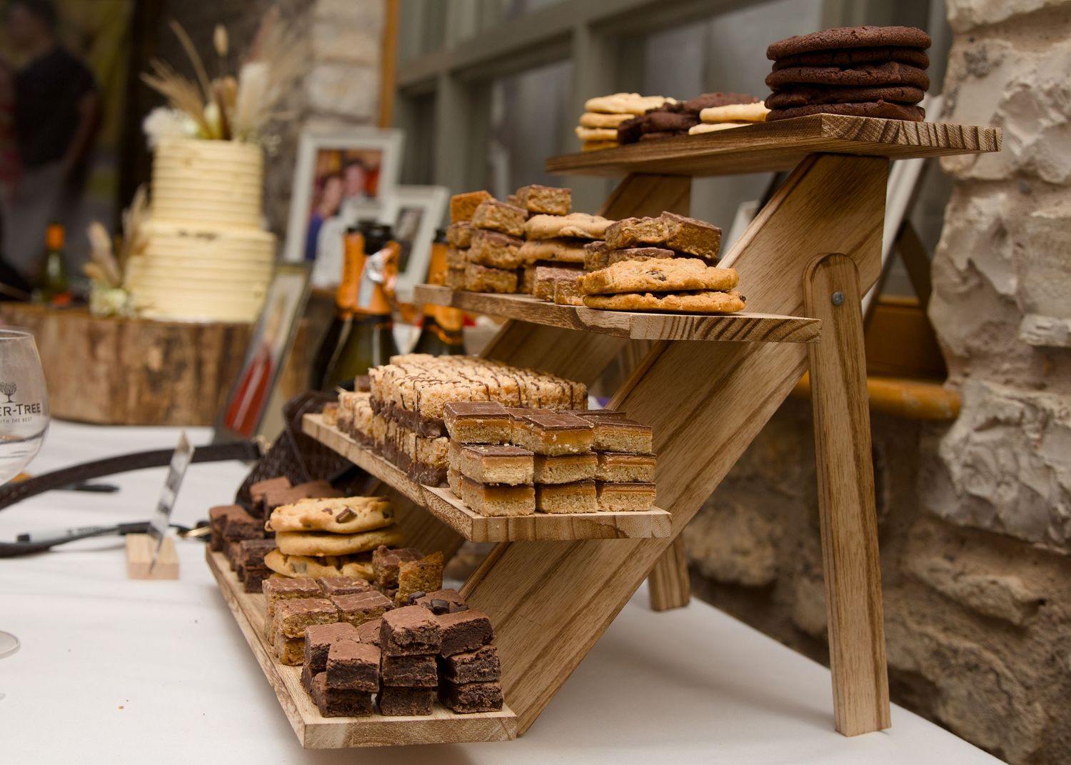 Tiered wooden display of assorted cookies and desserts at a wedding reception.