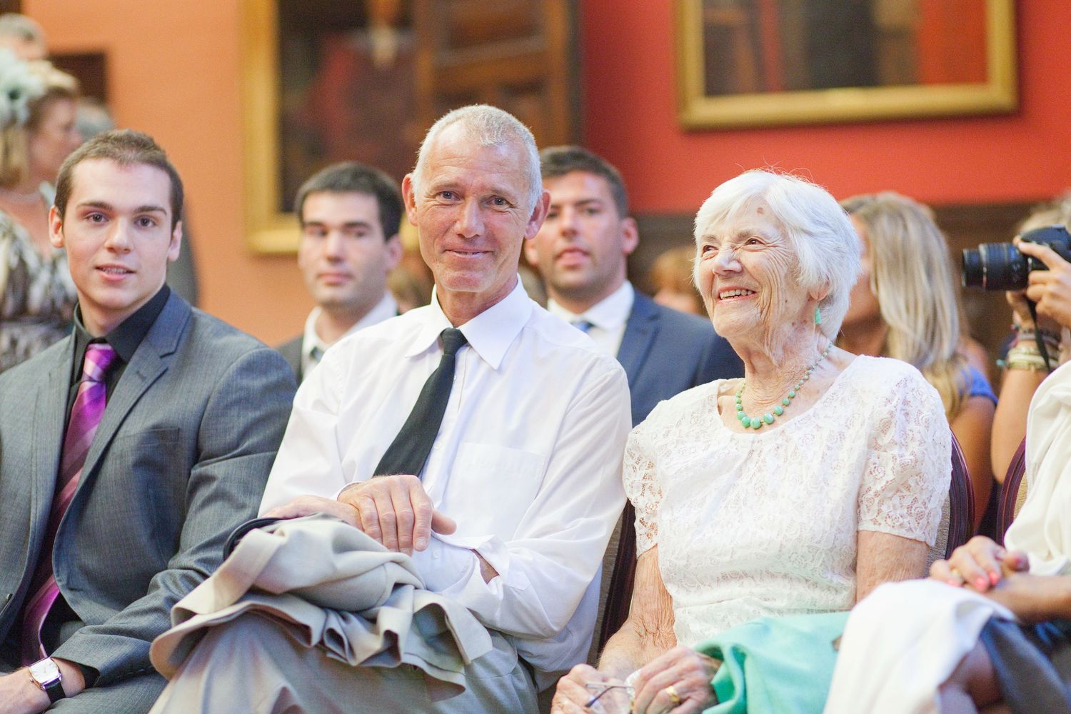 Wedding guests watching the ceremony from cushioned chairs in an elegant indoor setting.