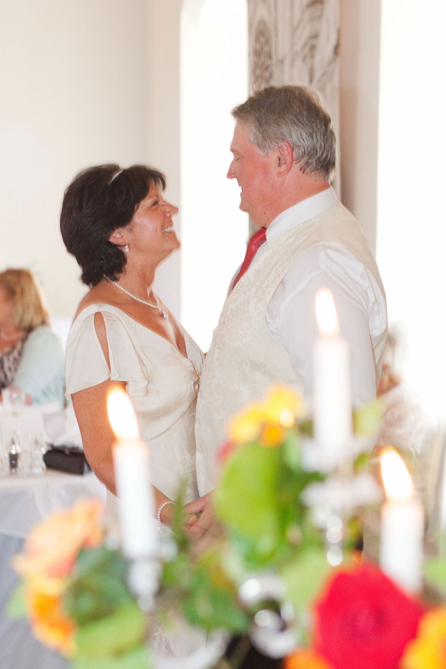 Wedding celebration with dancing couples and colorful floral decorations in an elegant white venue.