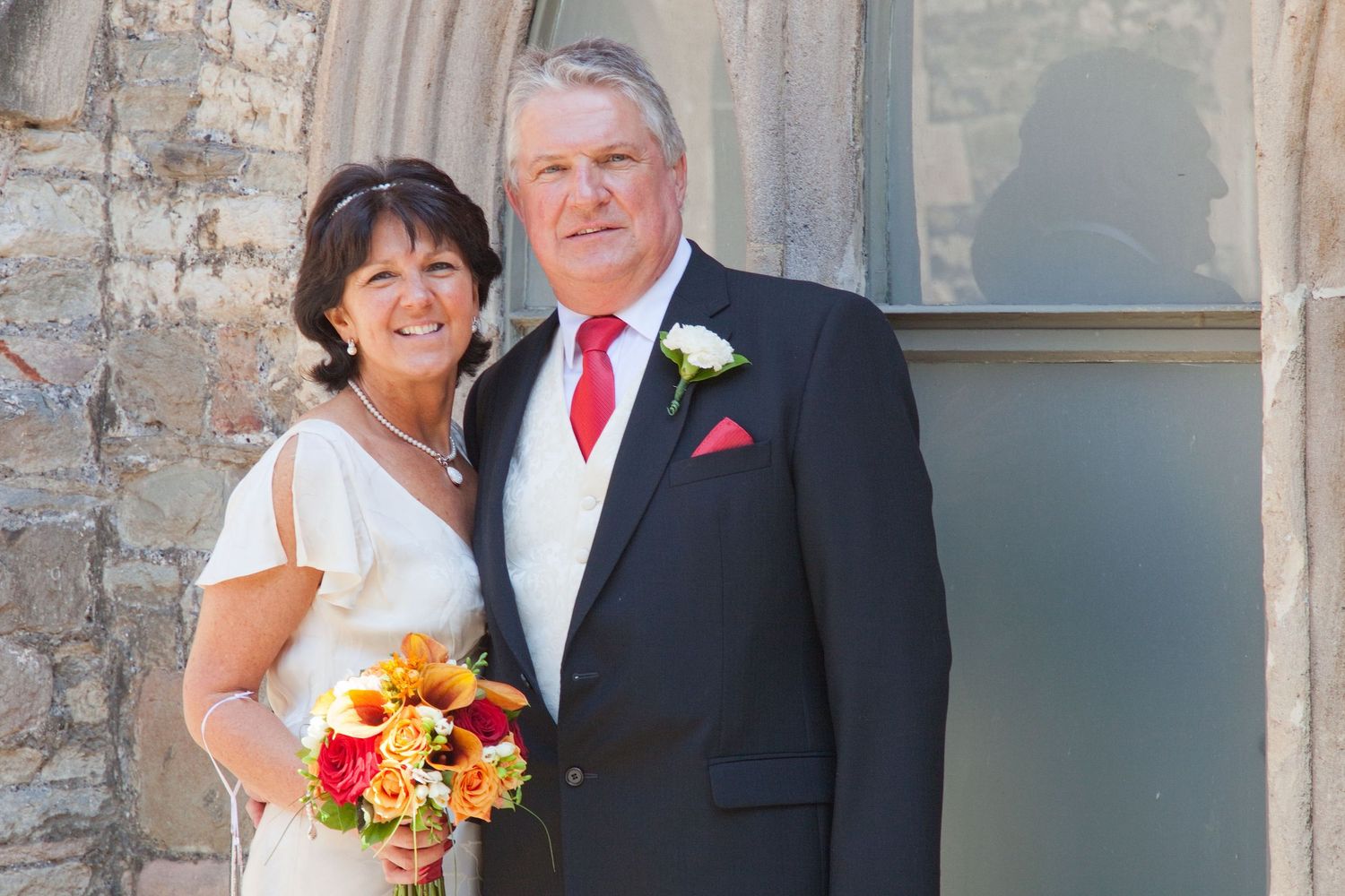 Newlyweds stand together against rustic stone wall backdrop.