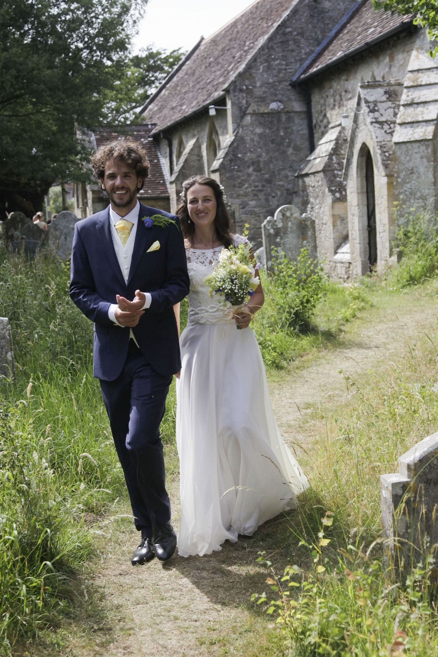 A bride and groom explore the grounds of a historic stone church.