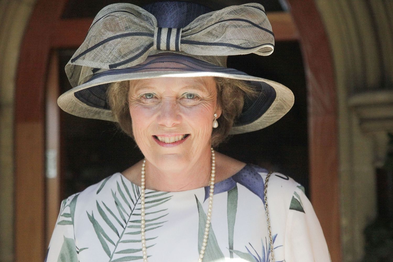 Wedding guests wearing elegant wide-brimmed hats gather outdoors.