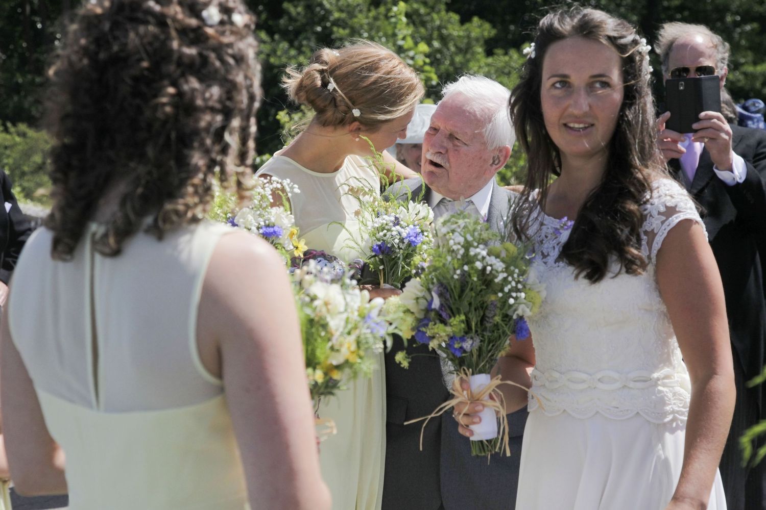 A group gathers outdoors holding bouquets of blue and white flowers during a celebration.
