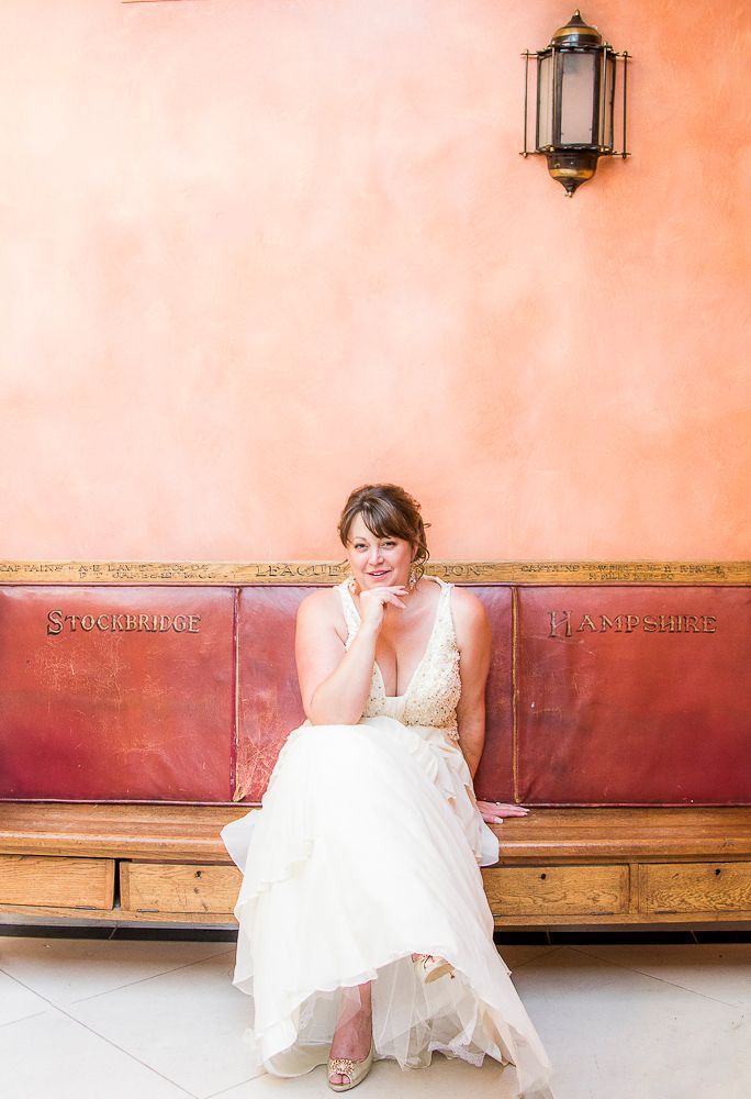 Bride sitting on wooden bench against coral colored wall.