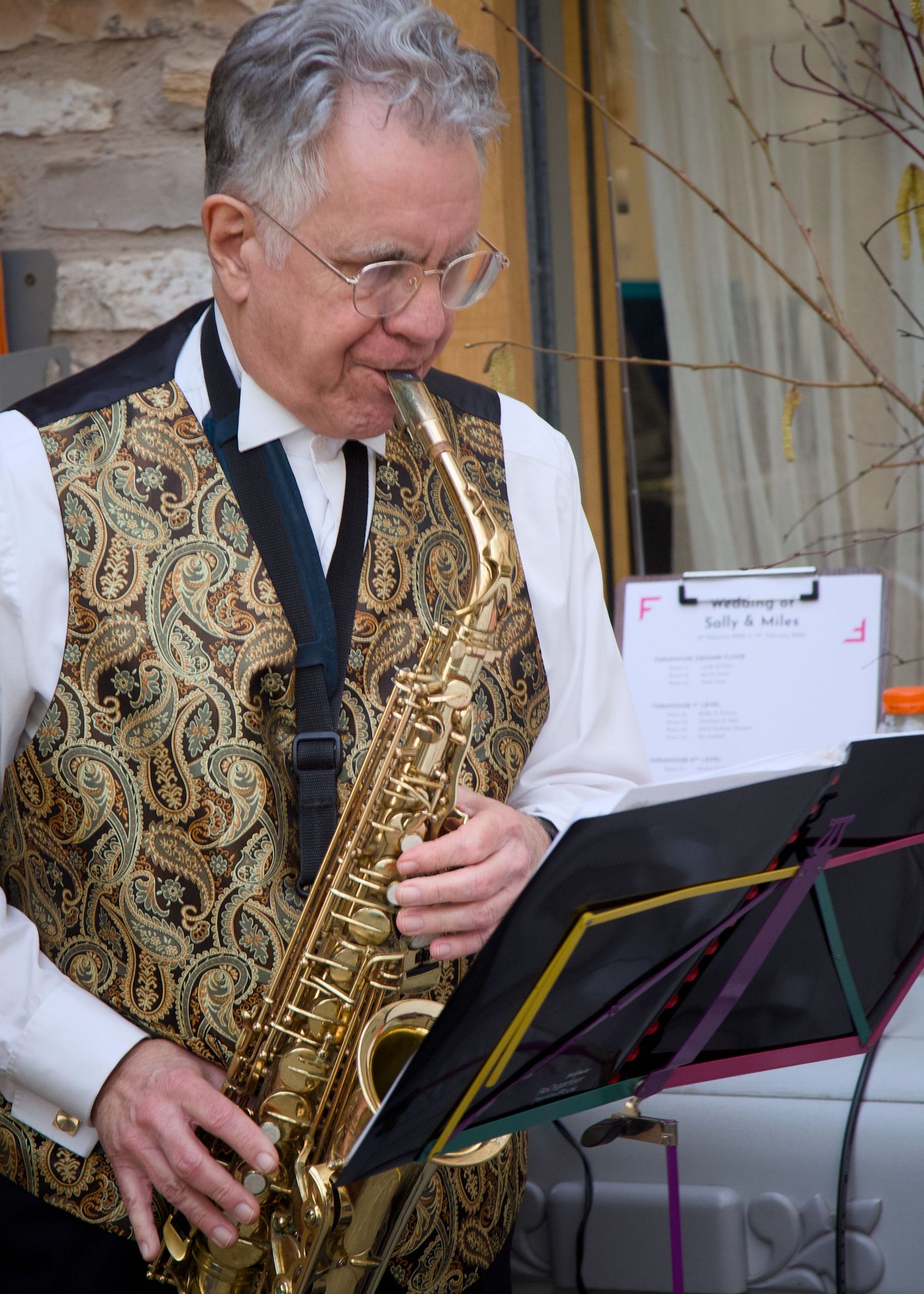 Musician playing saxophone at Folly Farm Somerset wedding in ornate gold vest performs with sheet music at outdoor wedding venue.