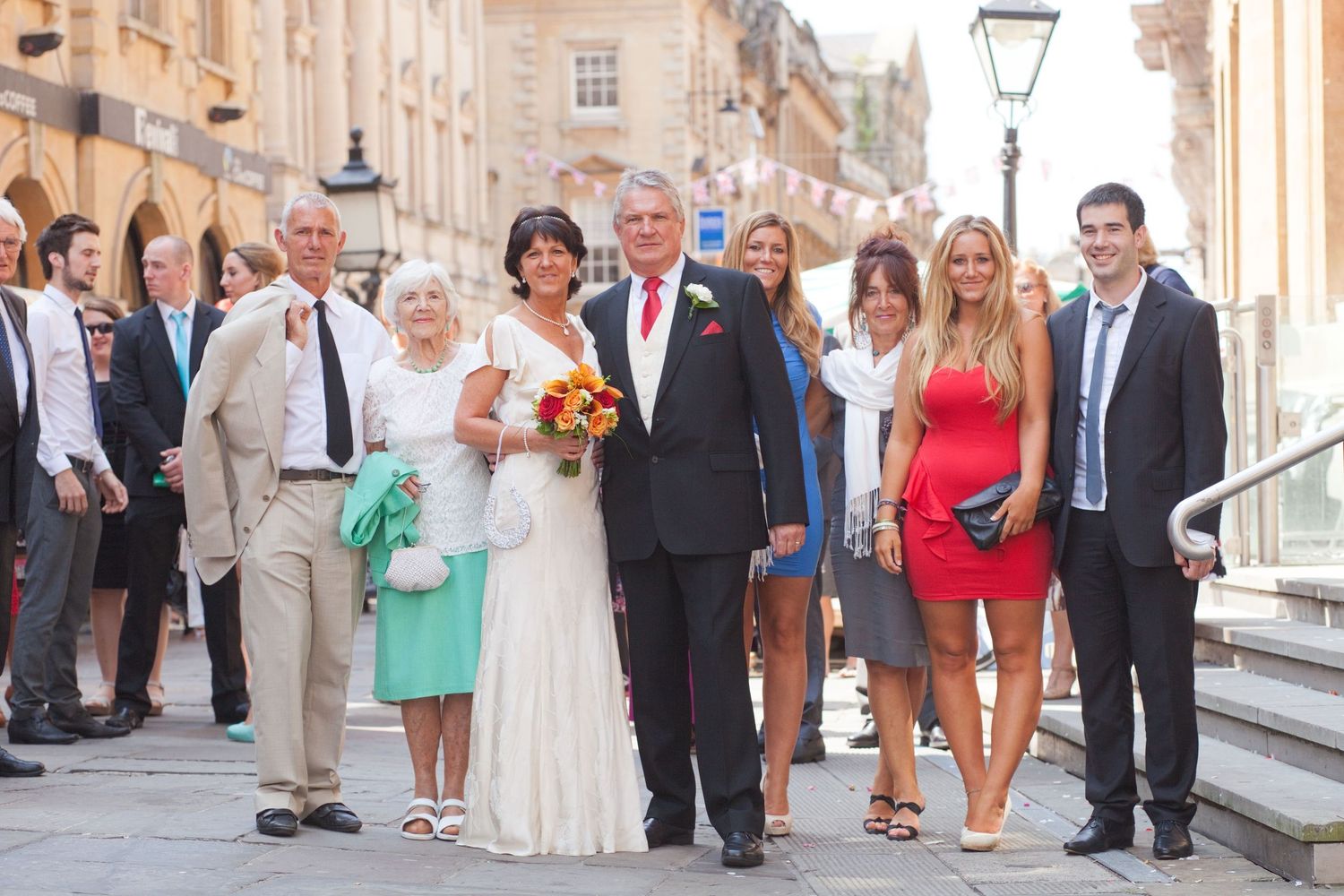 Wedding celebration with guests gathered along a historic street with stone buildings.