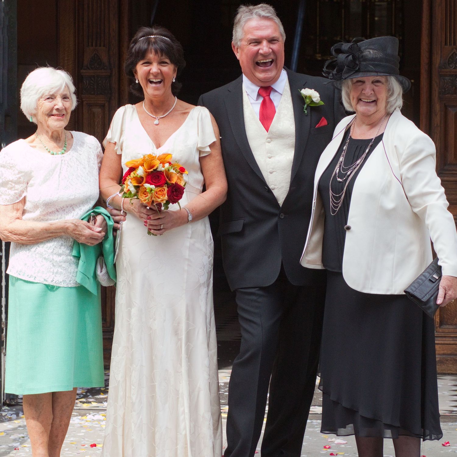 A wedding party group photo outside a building with the couple and elderly relatives.