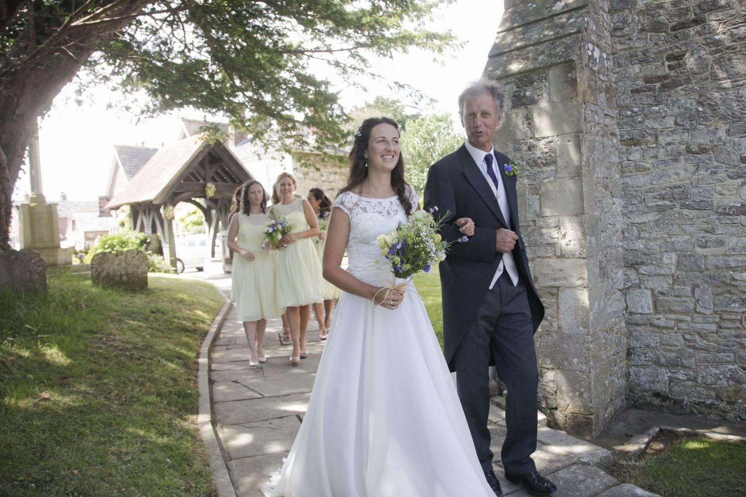 Wedding processional walking along stone path with traditional church architecture in background.