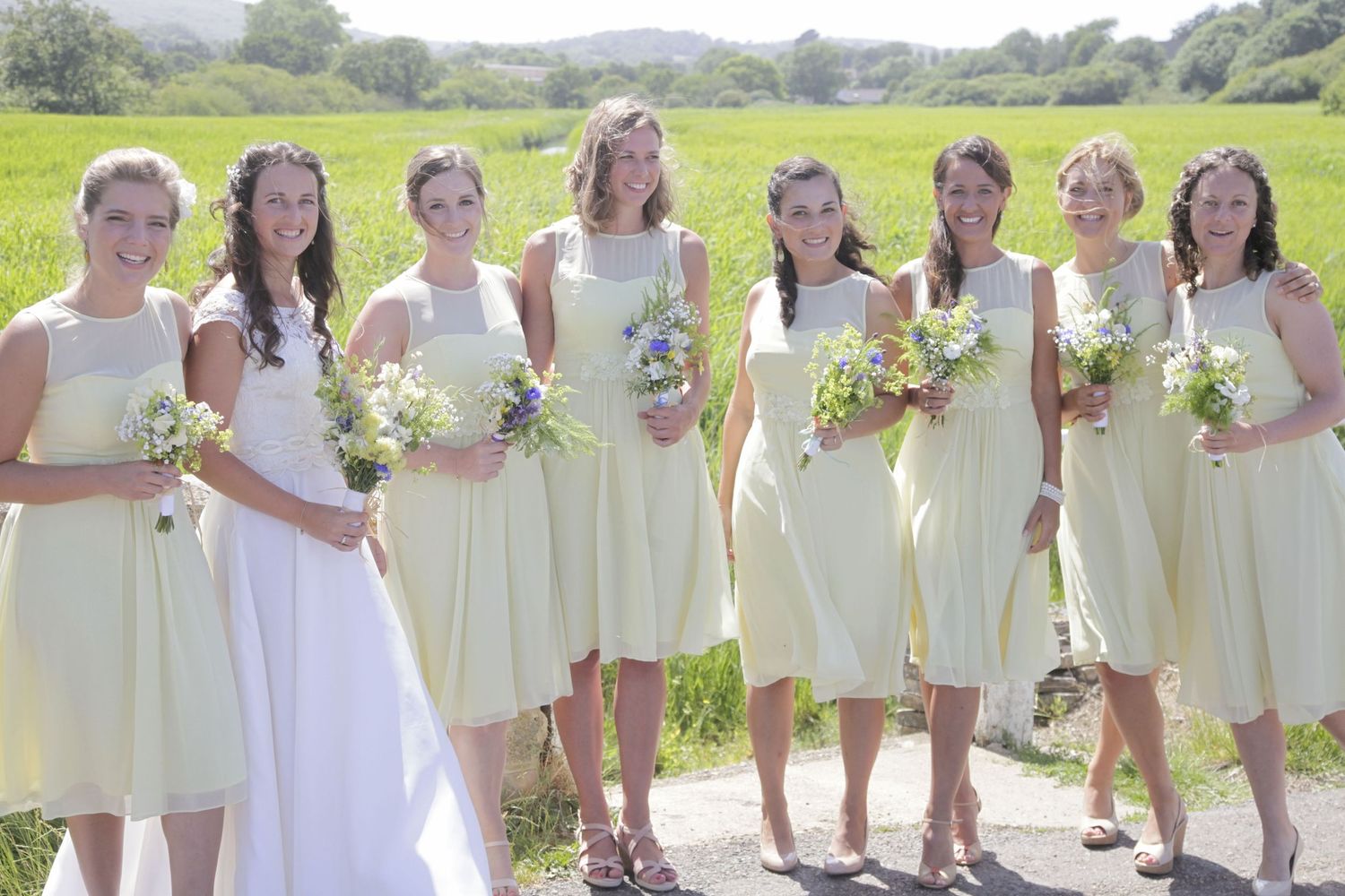 Bridal party wearing cream dresses poses together on a scenic country path.