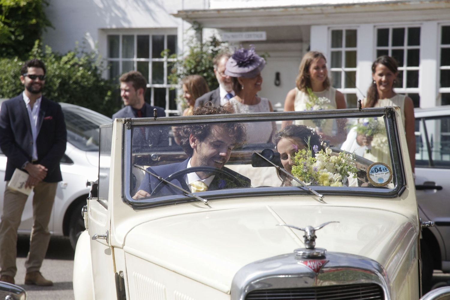 Vintage cream Rolls Royce parked outside traditional brick building during wedding event.