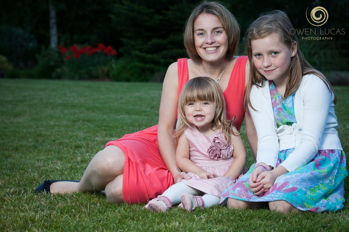 Family group relaxes together on green grass during outdoor summer photo session.