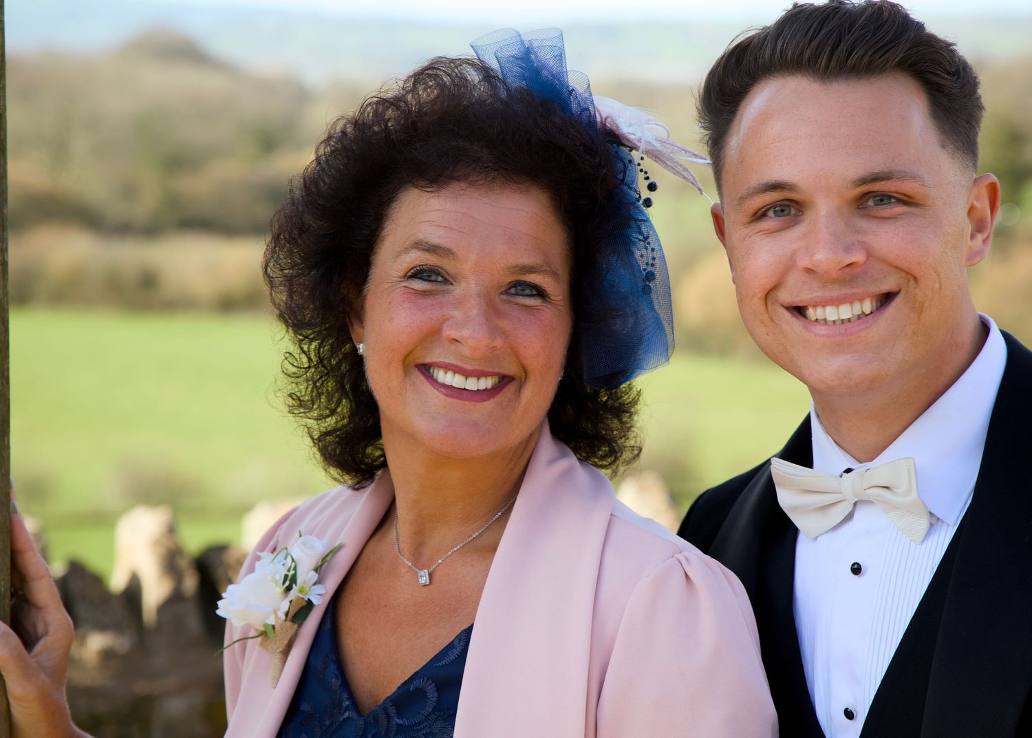 Wedding party members in formal attire pose outdoors against a scenic countryside backdrop.