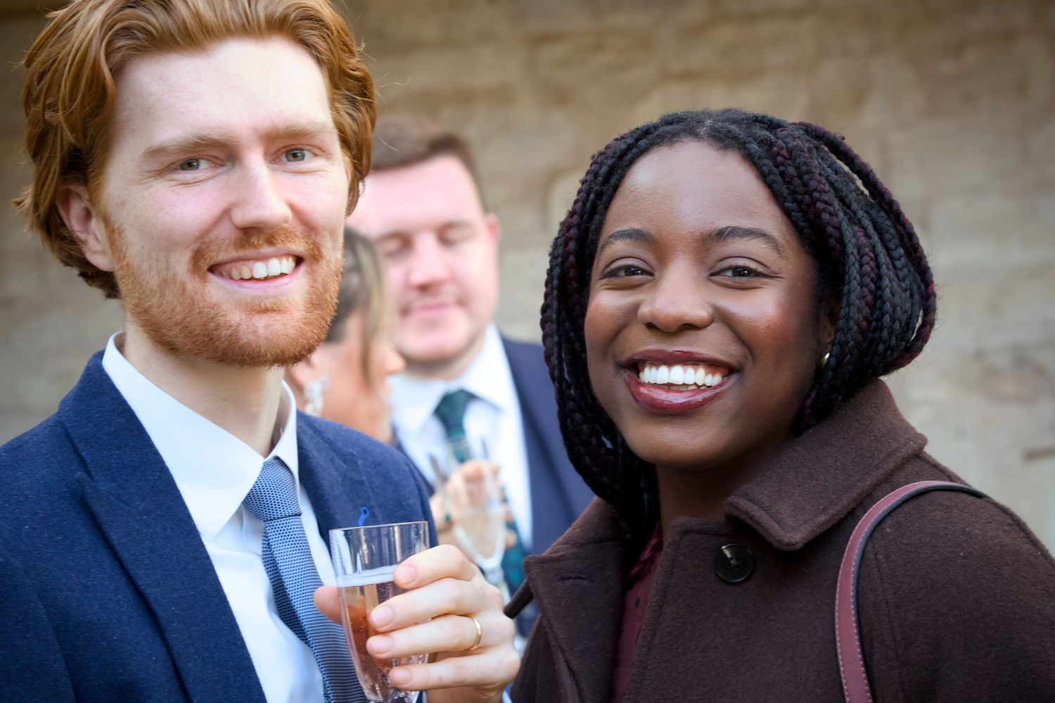 Two wedding guests share a laugh while enjoying drinks at an outdoor reception.