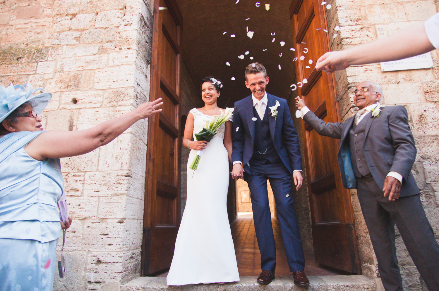 Wedding celebration with confetti being thrown in front of historic stone entrance.