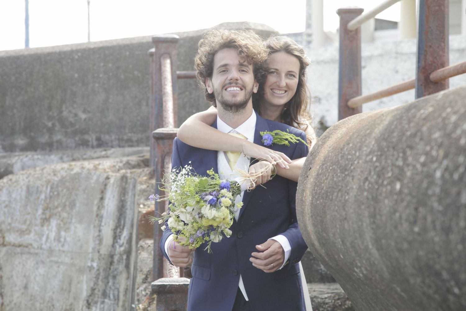 Joyful wedding couple embraces on stone walkway overlooking the ocean.