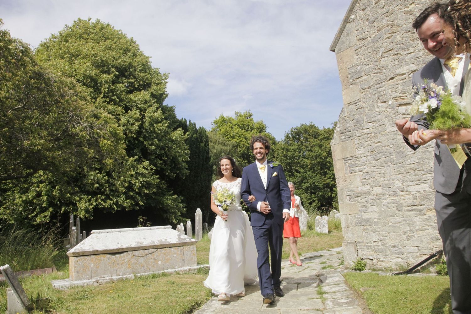 Wedding celebration taking place outside a historic stone building on a sunny day.