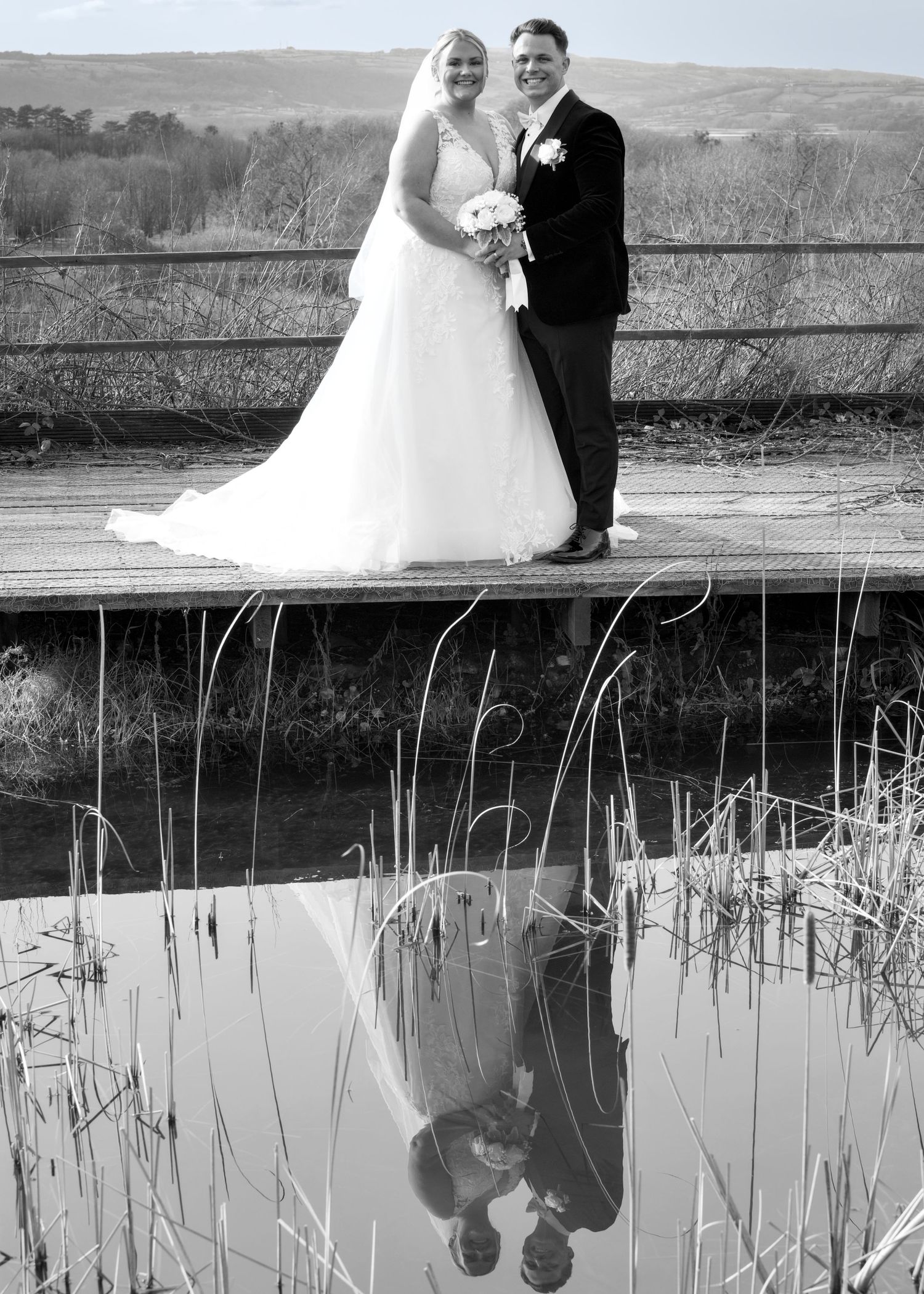 Black and white wedding photo of a couple on a deck with their reflection in a pond below.