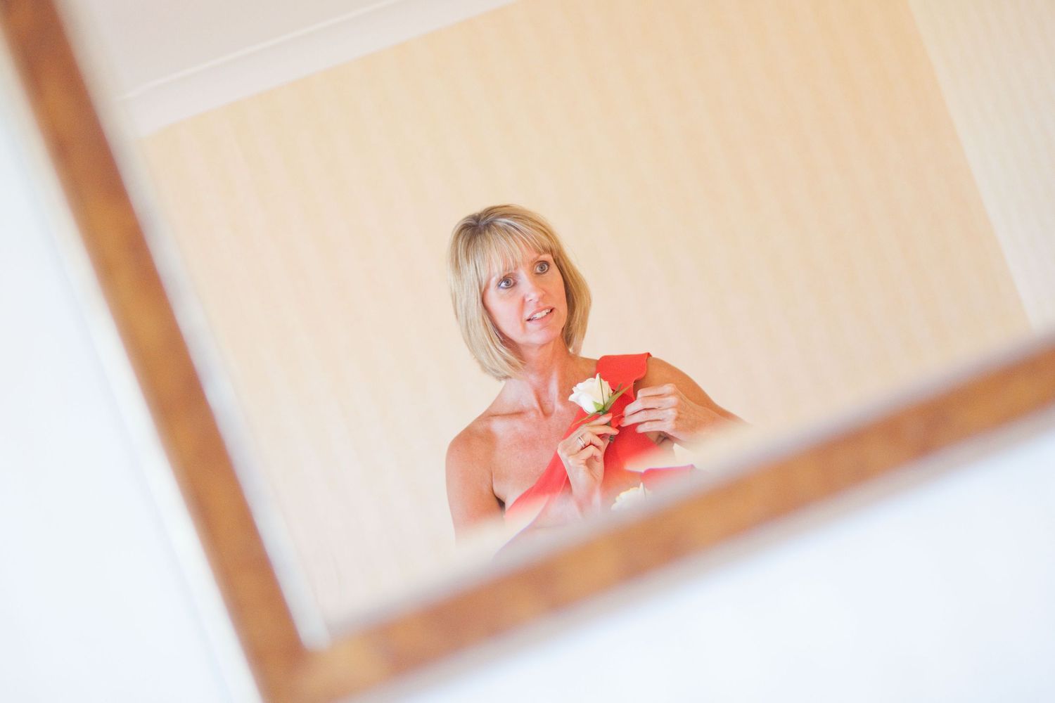 A reflection in a mirror shows someone wearing coral-colored attire with a boutonniere.
