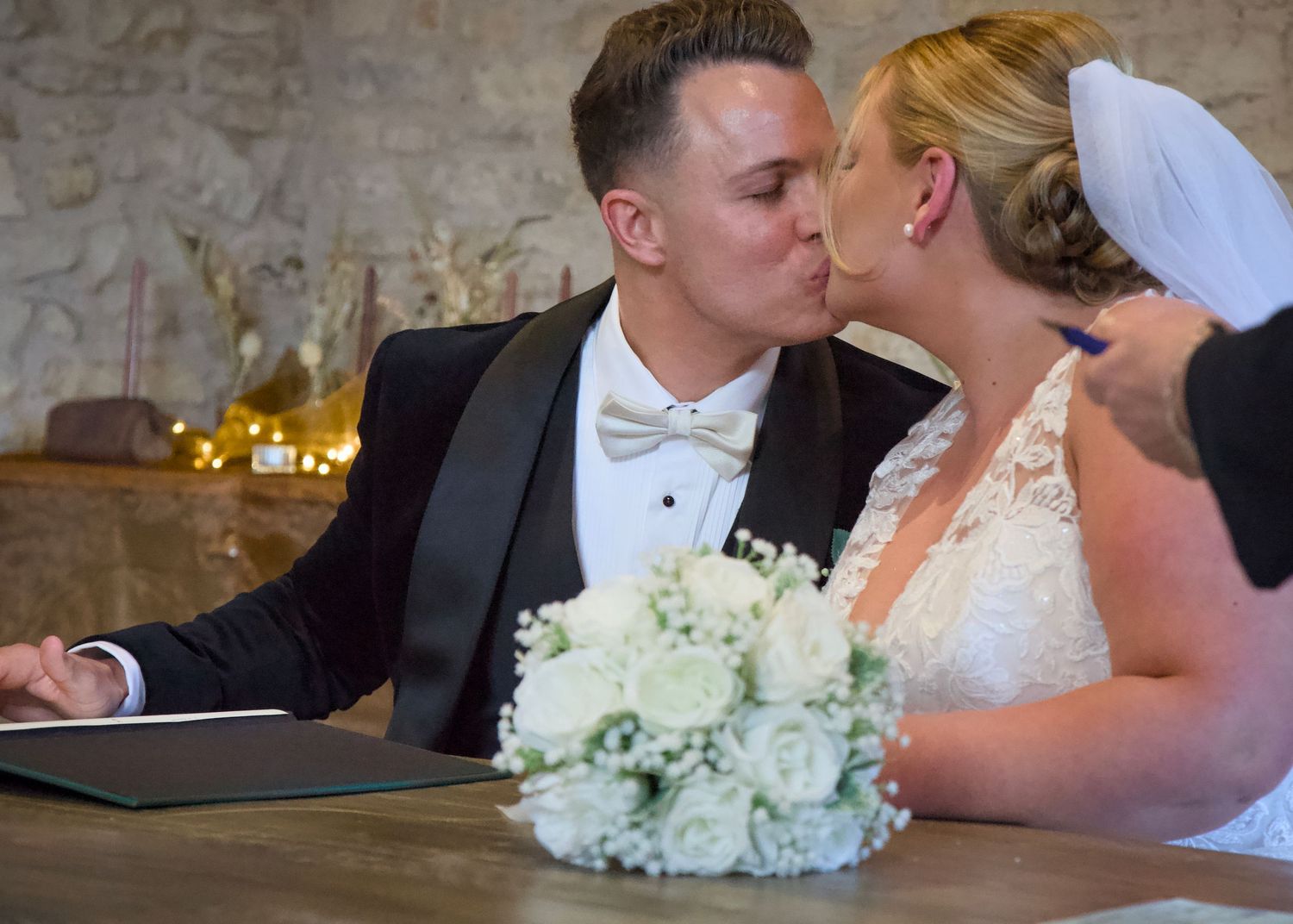 A romantic moment between newlyweds with a white bridal bouquet on a wooden table.