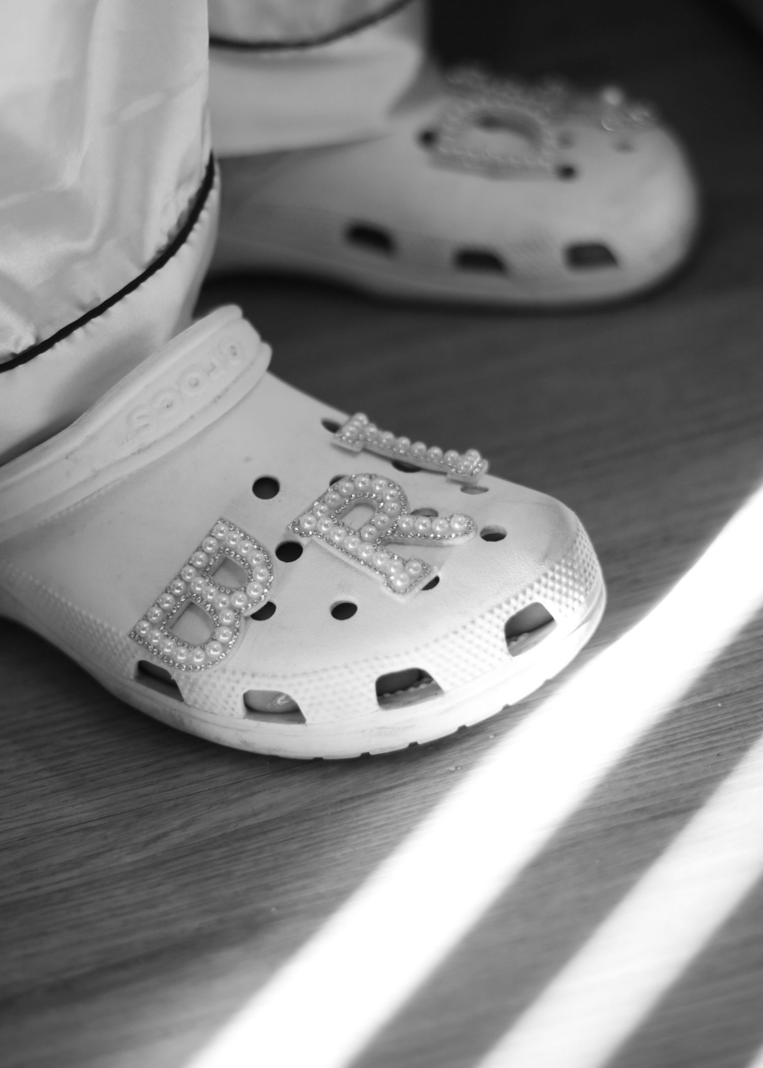 White Crocs shoes with decorative charms photographed in dramatic lighting on a wooden floor.