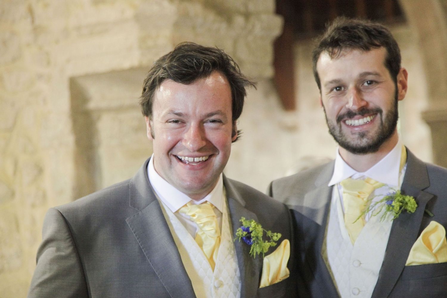 Group of groomsmen wearing matching suits and yellow ties pose under stone architecture.