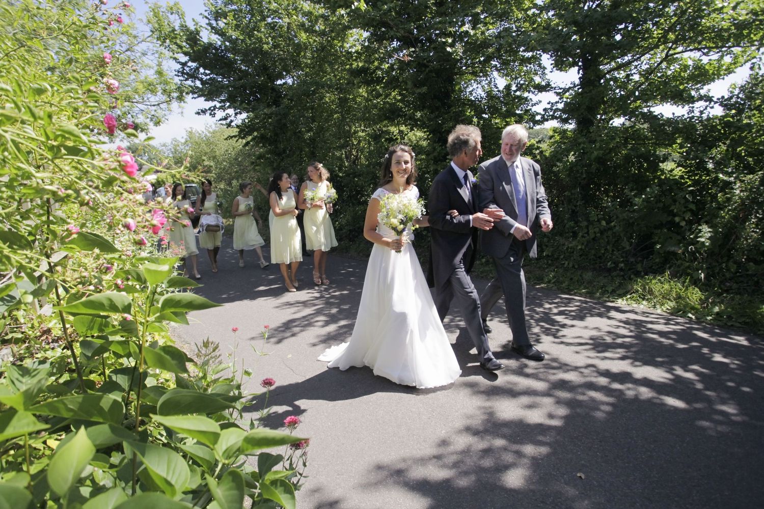 Wedding party walking down a tree-lined path during an outdoor ceremony.