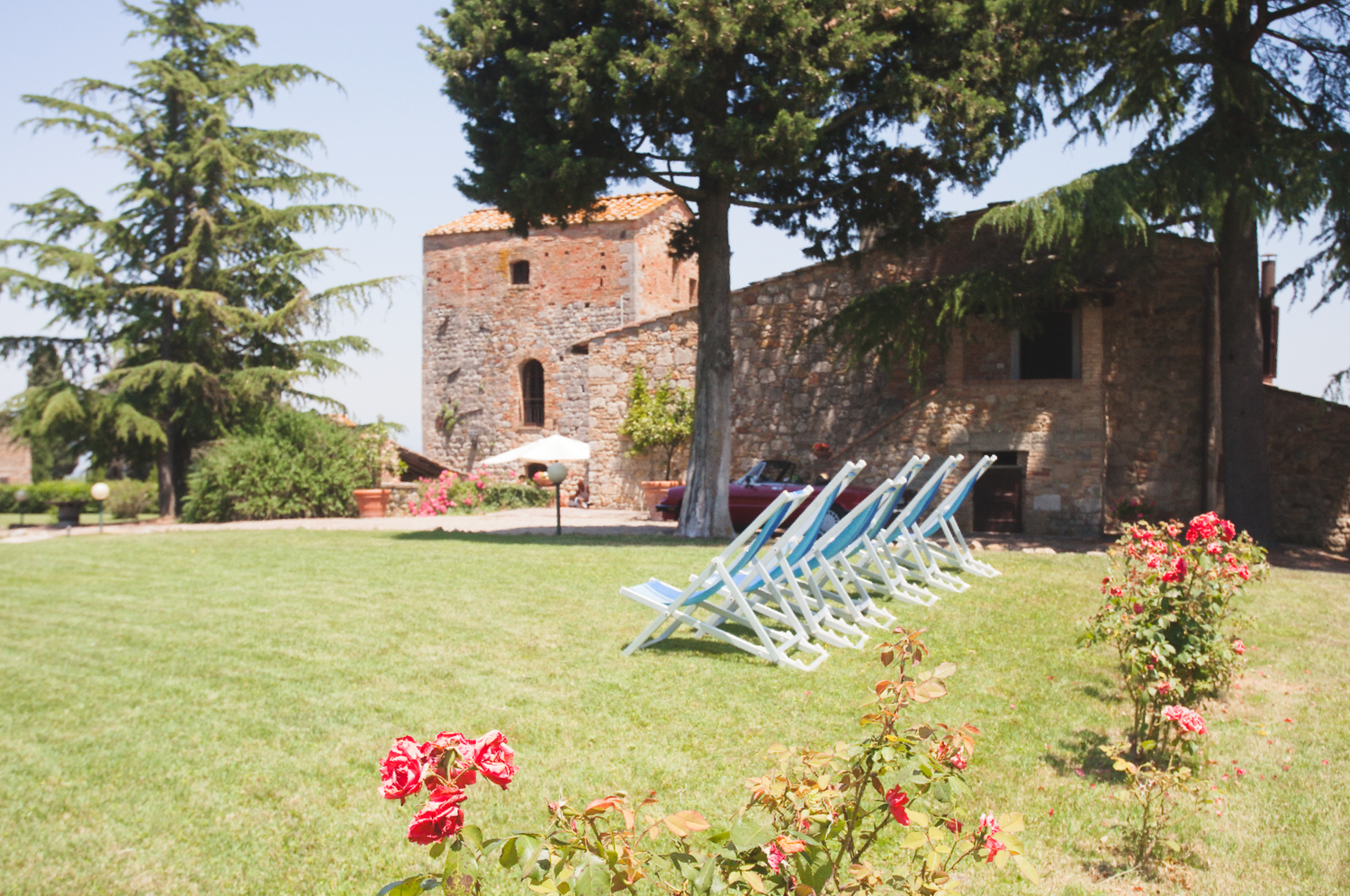 Panoramic view of a Tuscan villa garden with deck chairs and flowering plants.