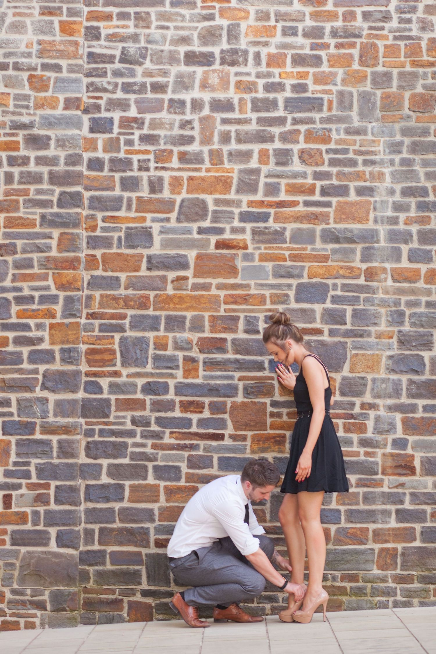 People in formal attire crouch along a rustic brick wall during an event.