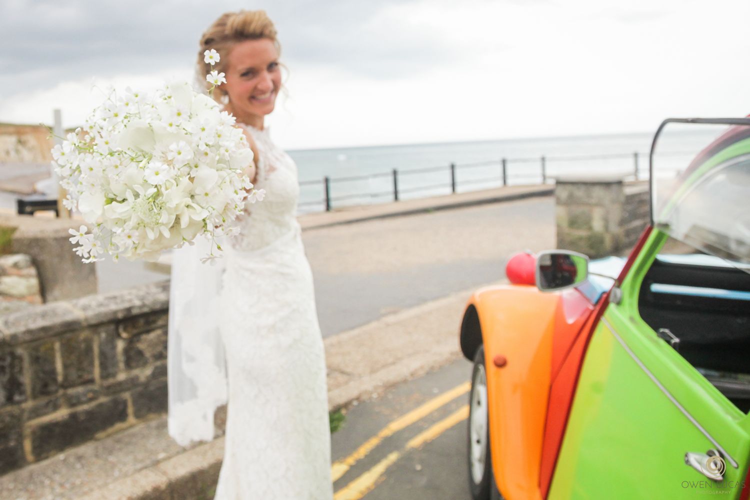 Wedding party poses with colorful beach surfboards and white floral arrangements by the ocean.
