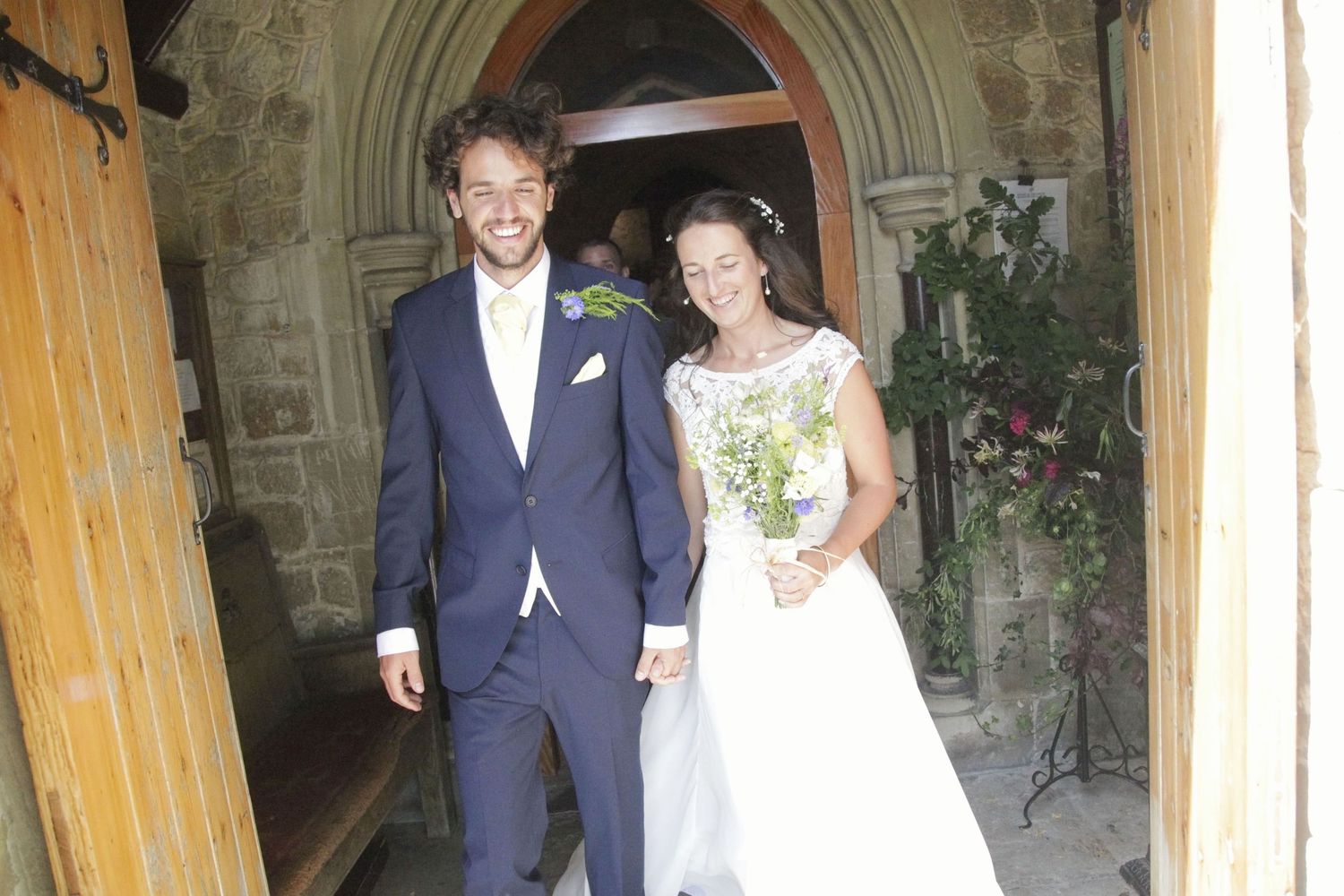 A wedding couple poses in front of a stone archway at a historic church.