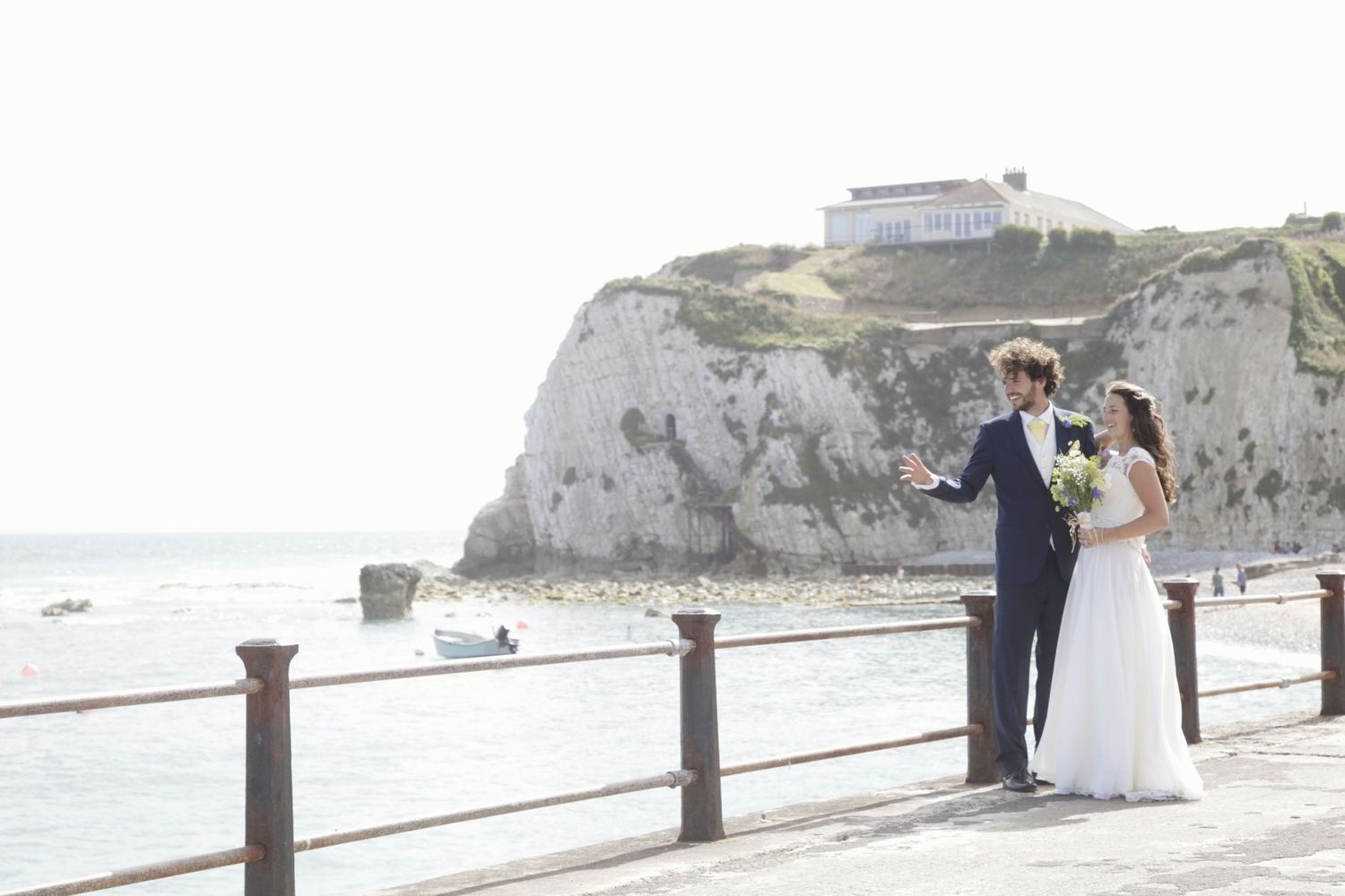 A wedding couple poses against dramatic coastal cliffs and ocean views on a bright sunny day.