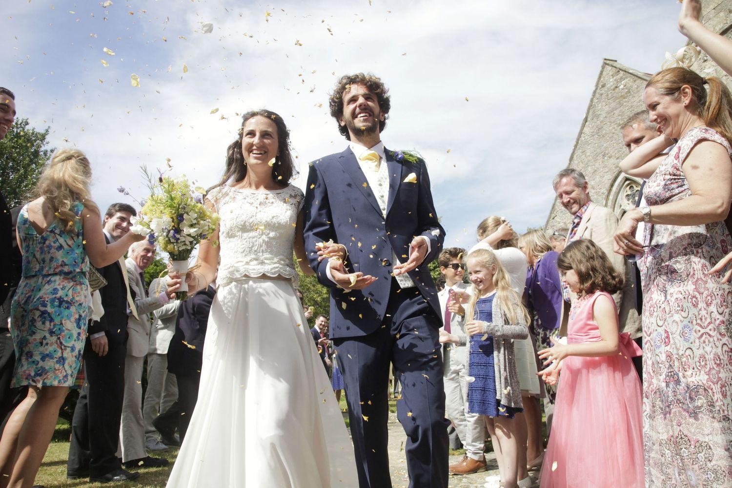Wedding party celebrates with traditional confetti toss outside church.